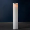 A tall, white LED candle with a flickering flame sits on a dark surface against a dark blue background. Náhľad obrázku produktu