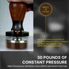 A hand is shown pressing down on a coffee tamper filled with coffee grounds, with text overlays explaining the pressure applied. Náhled obrázku produktu