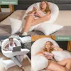 Collage of three images showing a woman using a large U-shaped pillow in different settings: relaxing in bed, sitting on a couch with a laptop, and reclining on a couch. Produktbild-Vorschau