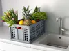 A grey folding crate filled with fresh produce and flowers sits on a kitchen counter next to a sink and faucet. Produktbild-Vorschau