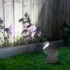 A dark gray LED spotlight illuminates purple flowers and a wooden fence in a garden at night. Produktbild-Vorschau