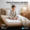 A young boy sitting on a bed with a white sheet, pillows, and a blanket. Anteprima dell’immagine prodotto