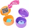 Two open toy capsules, one orange and one purple, each containing a small toy accessory. A pink arrow with text points to the orange capsule. Náhľad obrázku produktu
