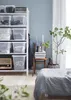 A bedroom scene with a shelf of storage boxes, a chair with books, and a bed. Voir les images du produit