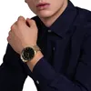 A close-up shot of a person wearing a dark blue shirt and a gold watch on their left wrist. Anteprima dell’immagine prodotto