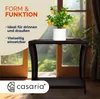 A small potted plant with yellow fruits sits on a dark brown polyrattan side table in front of a window with a garden view. Anteprima dell’immagine prodotto
