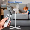 A hand holding a remote control is in the foreground, with a white stand fan and a child in the background. Produktbild-Vorschau