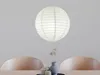 A white paper lantern hanging above a table with two chairs visible. Anteprima dell’immagine prodotto