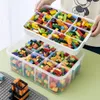 A person is holding a clear plastic storage box filled with colorful building blocks over another similar box. Produktbild-Vorschau