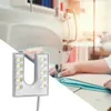 A sewing machine light is shown in the foreground, with a sewing machine and a person sewing in the background. Podgląd zdjęcia produktu