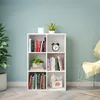 A white cube bookshelf filled with books and decorative items, placed against a light blue wall. Voir les images du produit