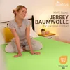 A woman sitting on a bed with a green sheet. Produktbild-Vorschau
