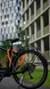 A bicycle lock is attached to a bicycle parked outdoors in front of modern buildings. Náhled obrázku produktu