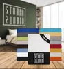 A stack of colorful fitted sheets is displayed in front of a bedroom scene with a bed and a wall graphic. Produktbild-Vorschau