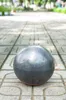 A gray garden sphere sits on a tiled walkway in a park-like setting. Anteprima dell’immagine prodotto