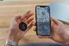 A person is holding a black key finder and a smartphone displaying a map with the key finder's location. Podgląd zdjęcia produktu