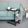 A small, dark brown side table with a metal frame and wheels is placed next to a light green sofa. A magazine rack is attached to the side of the table, holding several magazines. A white mug and an open magazine are on the tabletop. Náhľad obrázku produktu