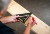 A person is using a black triangular ruler to mark a wooden plank. Voir les images du produit