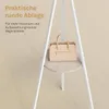 A beige handbag is placed on a round shelf of a white coat rack. Náhľad obrázku produktu