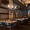 A dimly lit restaurant or bar interior with tables and chairs set up, featuring a vintage-style pipe wall lamp. Náhled obrázku produktu