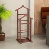 A wooden valet stand is shown in a room with a plant and a chair in the background. Produktbild-Vorschau