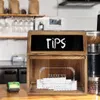 A wooden tip box with a chalkboard top is shown on a counter in what appears to be a cafe or restaurant setting. Náhled obrázku produktu