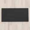 A black shower tray is shown from a top-down view, placed on a light-colored wooden floor. Produktbild-Vorschau
