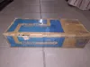 A cardboard box with blue and yellow branding, likely containing a printer toner cartridge, is placed on a tiled floor. Voir les images du produit