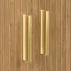A close-up view of two gold handles on a wooden cabinet with vertical grooves. Produktbild-Vorschau