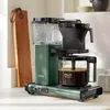 A green Moccacoffee maker sits on a countertop next to a wooden cutting board. Náhled obrázku produktu