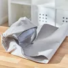 A glass object wrapped in gray packing paper on a wooden surface, with white shelving units in the background. Produktbild-Vorschau