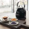 A black KitchenAid kettle is placed on a counter next to a brownie and small dishes of ingredients. Produktbild-Vorschau