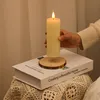 A hand holding a cream-colored LED candle above a book on a table. Voir les images du produit
