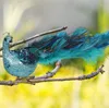 A decorative peacock ornament clipped to a tree branch. Produktbild-Vorschau