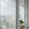 A view through a partially open sliding glass door onto a balcony with outdoor furniture and a plant. Produktbild-Vorschau