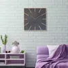 A square wall clock with a dark face and wooden hour markers is mounted on a white brick wall above a purple sofa and a white shelf unit. Náhled obrázku produktu