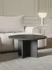 A round coffee table in front of a textured couch, with a lamp on a side table in the background. Anteprima dell’immagine prodotto