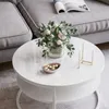 A round white coffee table with a vase of flowers and a small bowl of candies on it, next to a grey sofa. Produktbild-Vorschau