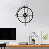 A modern black metal wall clock with a minimalist design is mounted on a white wall above a wooden desk with a computer monitor and books. Produktbild-Vorschau