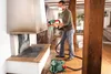 A man is using a paint sprayer to paint a fireplace in a room that is being renovated. Produktbild-Vorschau