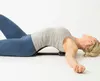 A woman is lying on her back on a white surface, using a back stretcher device. Produktbild-Vorschau