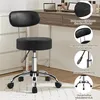 A black adjustable stool with a backrest is shown in a room, possibly a dressing room or studio, with a vanity table in the background. Produktbild-Vorschau