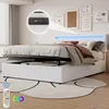 A white upholstered bed with a tufted headboard featuring LED lighting, shown with the storage compartment open. A remote control for the lighting is visible in the foreground. Náhled obrázku produktu