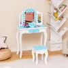 A child's vanity table and stool set with a tri-fold mirror, decorated with blue and white polka dots, is set up in a room with a bookshelf and a stool. Produktbild-Vorschau