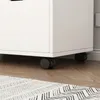 The bottom part of a white filing cabinet with black casters on a wooden floor with a rug. Podgląd zdjęcia produktu