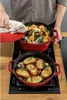 A person is cooking seafood and bread in two red cast iron pots on a stovetop. Produktbild-Vorschau