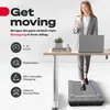 A woman is using a treadmill under a standing desk while looking at her phone. The image highlights product features with icons and text. Produktbild-Vorschau