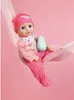 A baby doll in a pink outfit is sitting in a pink hammock. Náhľad obrázku produktu