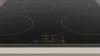 A close-up, eye-level shot of a black induction cooktop with four heating elements and a digital display showing cooking settings. Produktbild-Vorschau