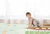 A baby is crawling on a play mat in front of a window with sheer curtains. Produktbild-Vorschau